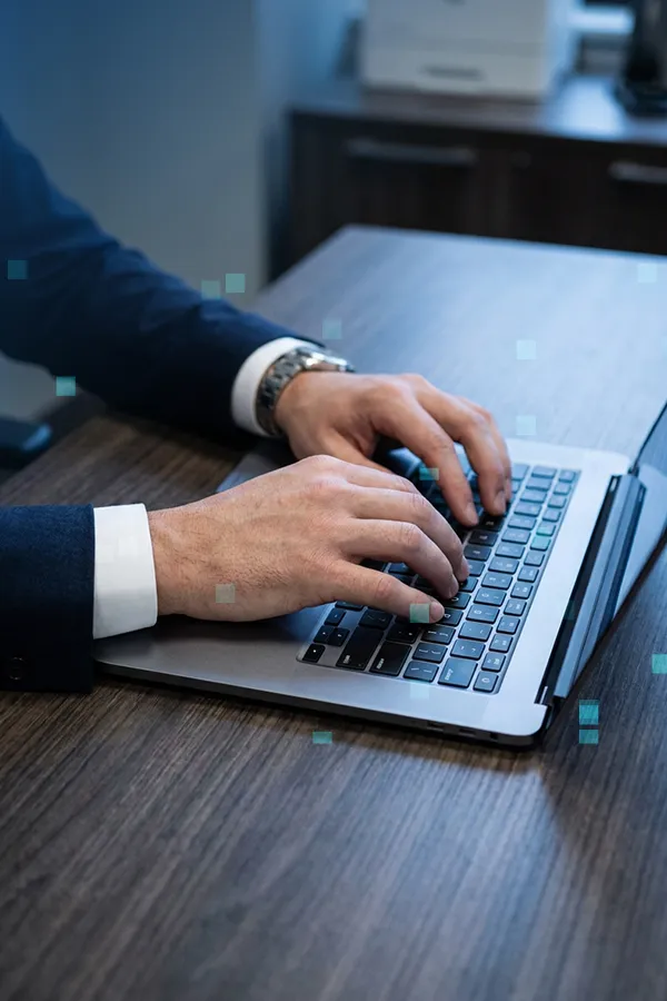A person in a warm mustard sweater typing on a laptop at a wooden desk